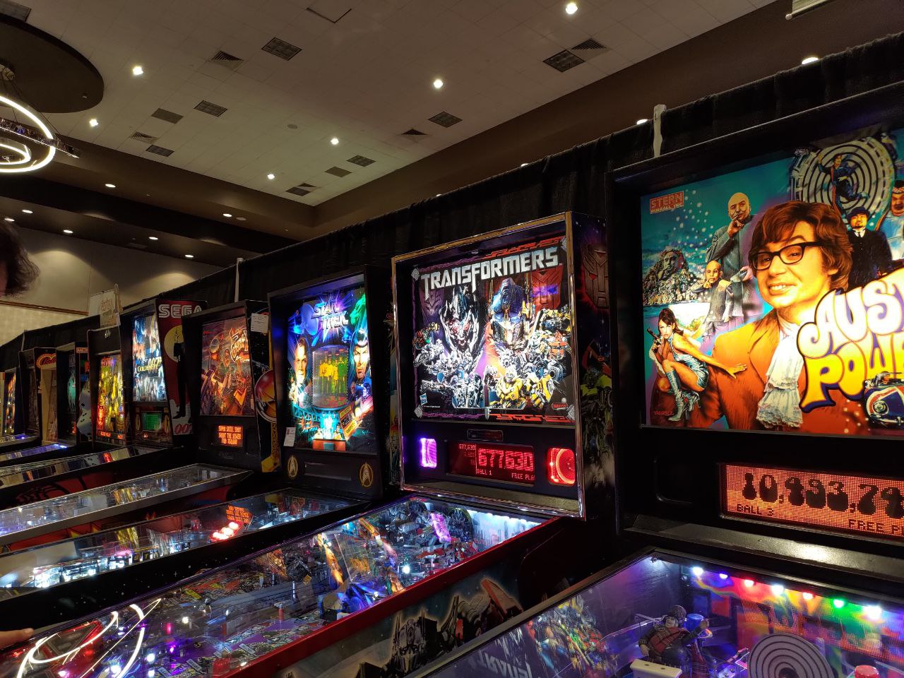 a bunch of pinball machines lined up in a row. Many of the machines are based on popular entertainment franchises, such as Austin Powers, Star Trek, and Transformers.